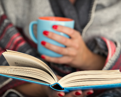 person holding open book and coffee mug